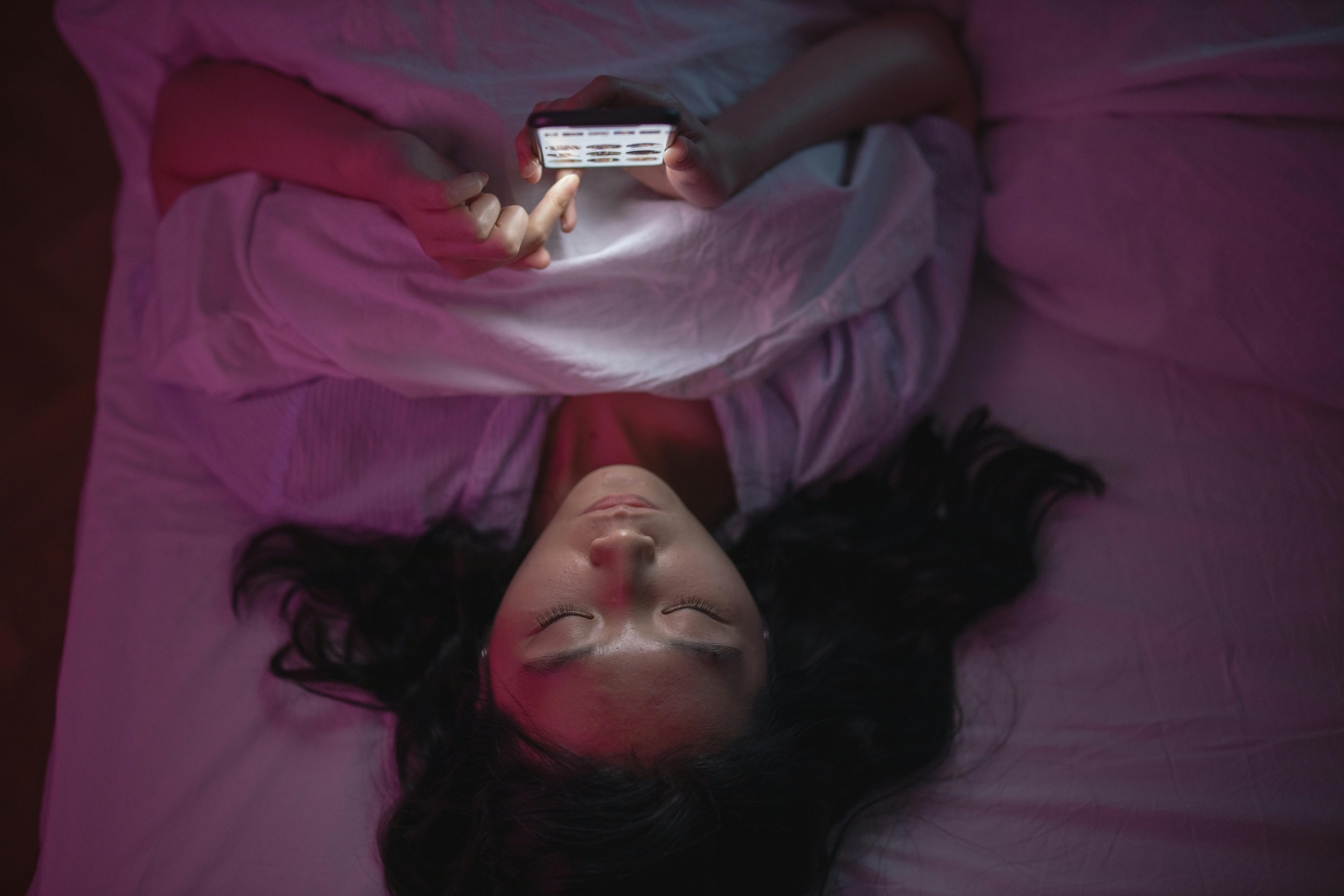Žena leží v posteli a prezerá si profily v online zoznamovacej aplikácii na mobile